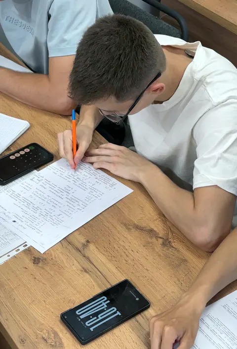 Ученик пишет контрольную работу на занятии, рядом на парте телефон с таймером
